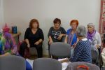 Zdjęcie przedstawia cztery moderatorki siedzące pod ścianą i jedną odwróconą do nich bokiem. Panie omawiają zadanie w trakcie warsztatów, które odbywają się w siedzibie WBP na ul. 1 Maja 5 w Olsztynie. Za nimi kremowa ściana, po lewej stronie stół z książkami.