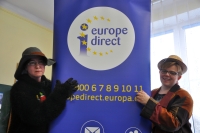 Aktorki przedstawienia stoją po dwóch stronach banneru. Napis z banneru: Europe Direct.