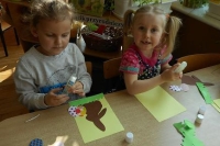 Na zdjęciu dwie dziewczynki siedzące przy biurku, przygotowujące wielkanocne ozdoby w formie papierowych króliczków.