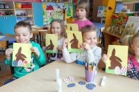 Na zdjęciu czworo dzieci siedzących przy biurku i prezentujących gotowe ozdoby wielkanocne w formie papierowych króliczków.