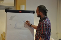 Na zdjęciu prowadzący Adam Cieślak stoi przed flipchartem, na którym pokazuje, jak wykonać poszczególne elementy rysunku.