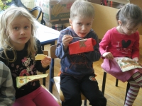 Trójka przedszkolaków siedzi na krzesłach. Dzieci trzymają serwetki i wykałaczki. Jedzą czekoladę.