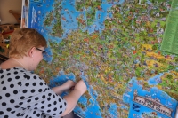 Zdjęcie przedstawia osobę prowadzącą zajęcia, która przymocowuje coś do mapy przedstawiającej Europę.