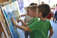 Czworo przedszkolaków stoi przy mapie Europy. Dzieci wskazują na mapę palcami.