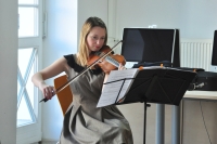 Na zdjciu znajduje si skrzypaczka Agnieszka Wojtkowiak, ktra gra koncert na skrzypcach. Siedzi na krzele. Przed ni, na stojaku znajduj si nuty.