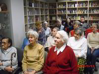 Zdjęcie 01: Pomieszczenie Muzoteki. Po lewej stronie i na wprost znajdują się regały. Na półkach płyty cd, dvd i audiobooki. Na krzesłach w czterech rzędach siedzą seniorzy z Centrum Alzheimera „Dar Serca” z Olsztyna.