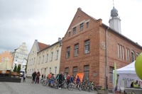 Zdjcie przedstawia budynek Starego Ratusza. Pod budynkiem ustawiona jest grupa cyklistw z rowerami.