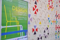 Zdjcie przedstawia plakat wydarzenia. Z prawej strony jeden z eksponatw: dywan z kolorowymi trjktami.