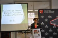 Za trybunk Pani Dorota Pale-Krajewska, dyrektor MBP w Lidzbarku Warmiskim prezentuje swoje wystpienie. Na ekranie po lewej stronie wywietlana jest prezentacja - wida slajd pocztkowy z tytuem wystpienia. Za mwic cianka WBP.