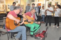 Przedstawiciele Stowarzyszenia „Stare buty” grajcy na gitarach w tle publiczno wernisau