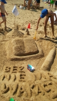 Na zdjciu zamek z piasku w ksztacie ksiki i napis z piasku „Bez ksiki nie ma wakacji”.