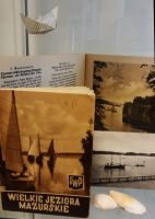 Cz ekspozycji: dwubarwna broszura „Wielkie Jeziora Mazurskie”, otwarty folder w jzyku niemieckim otwarty na ilustracji z aglwk, czarno-biaa widokwka przedstawiajca aglwki przy pomocie oraz dwie biae muszle may jeziornych